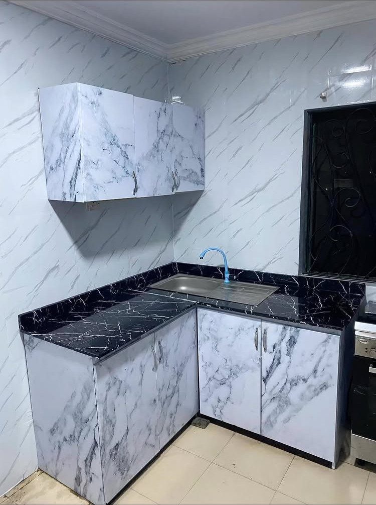 Marble-patterned white kitchen cabinets with black countertops and a stainless steel sink.