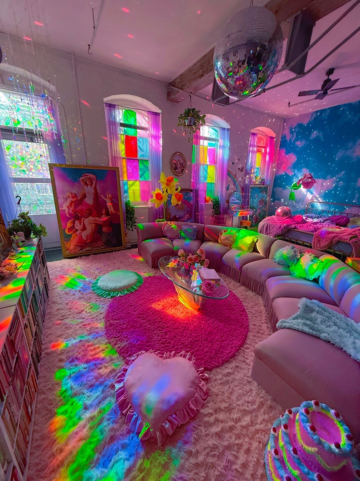 Pink maximalist room with a curved sofa, heart pillow, and colorful disco lighting.