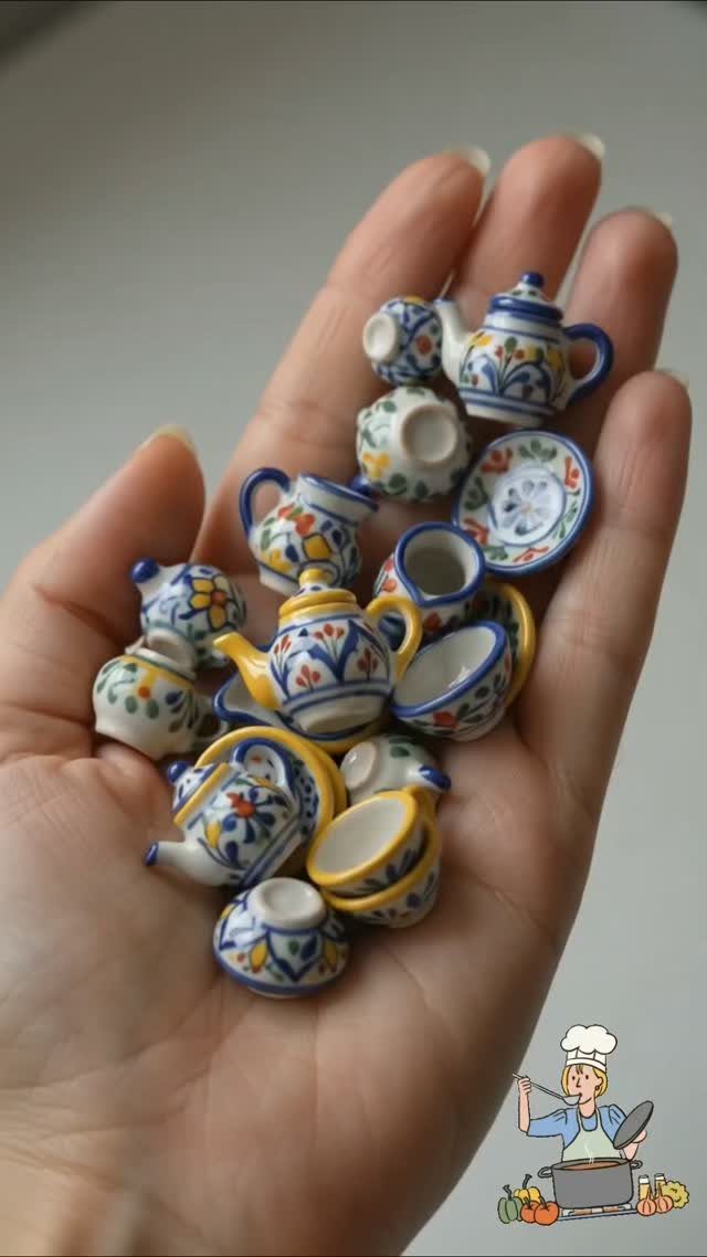 Miniature white ceramic tea set pieces with blue and yellow floral patterns in a hand.