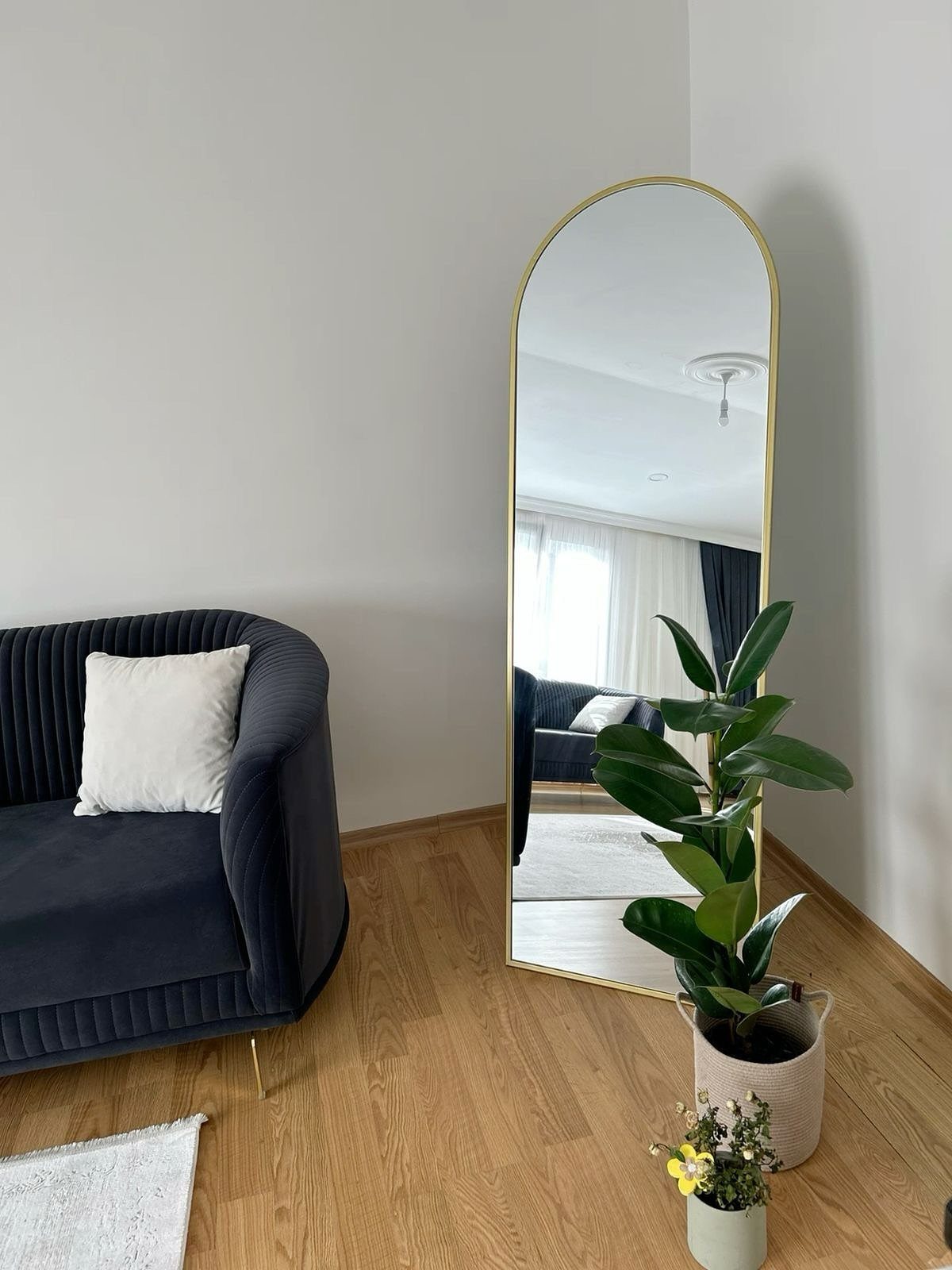 Arched gold mirror reflecting a bright window and white curtains in a living room.