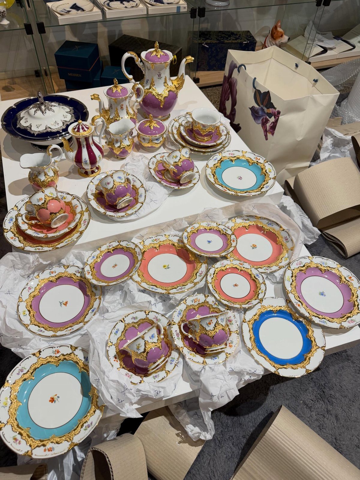 Vintage porcelain tea sets and colorful ornate plates arranged on a white table.