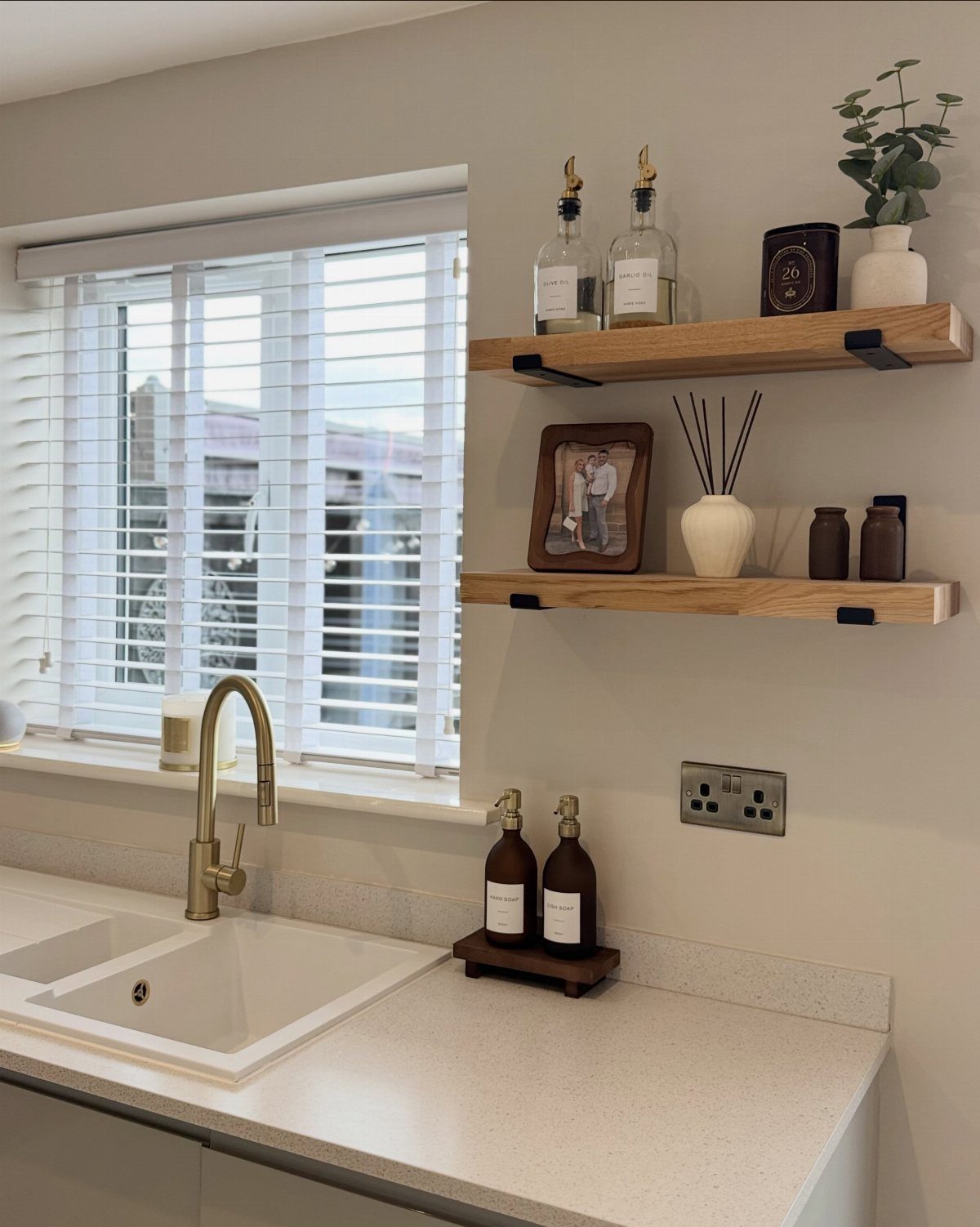 White kitchen countertop with gold faucet and light-wood floating wall shelves.