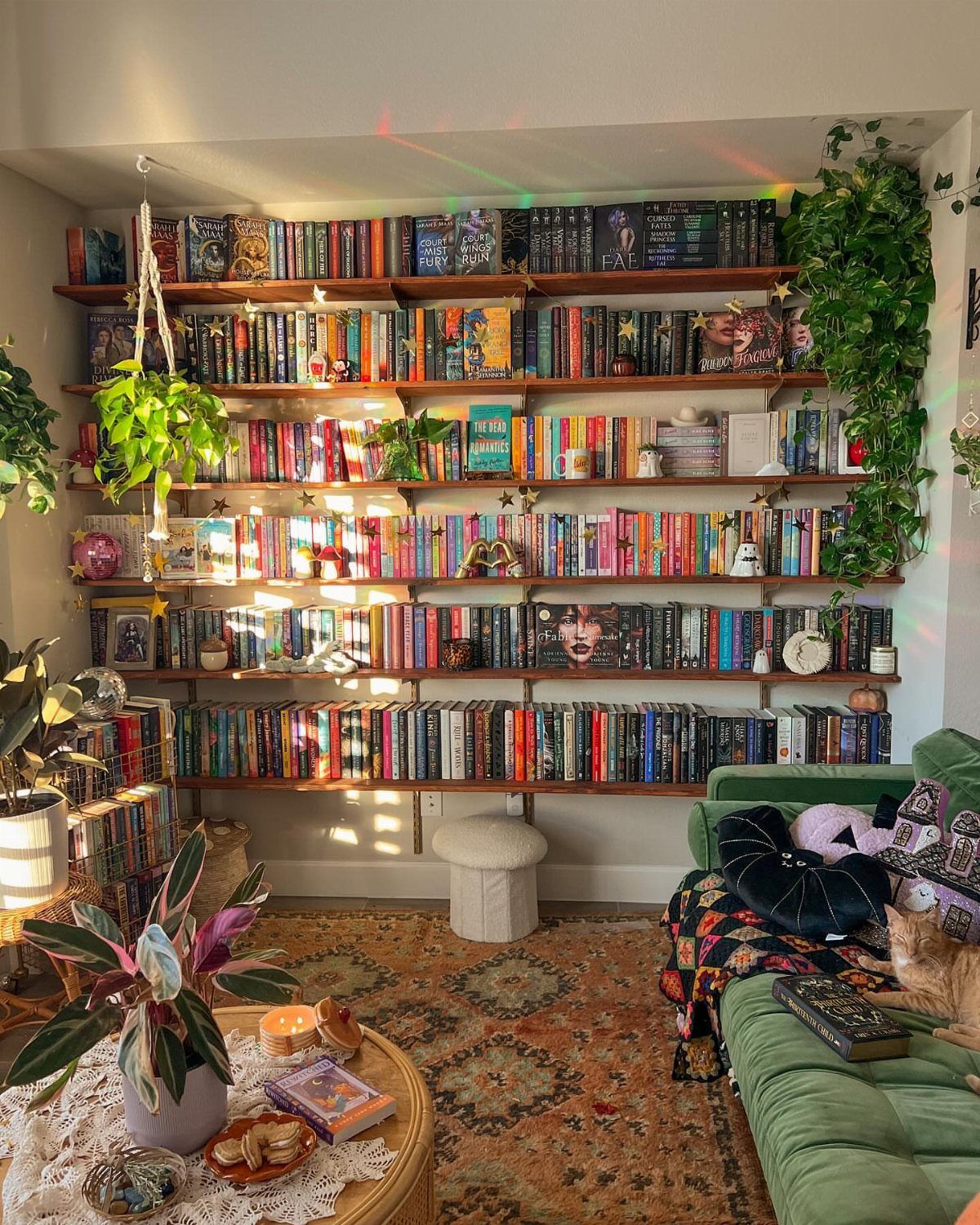 Bookshelves filled with colorful books above a green velvet sofa and patterned rug.