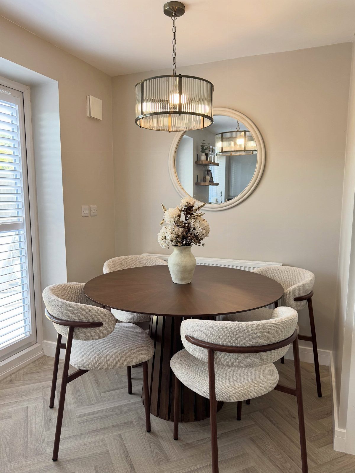 Round dark wood dining table with a pedestal base and white upholstered chairs.