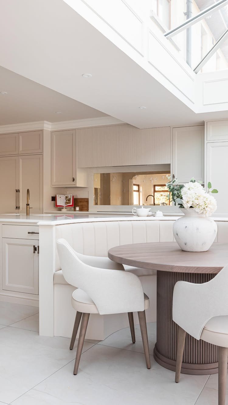 Round wooden pedestal dining table with white chairs and built-in banquette seating.