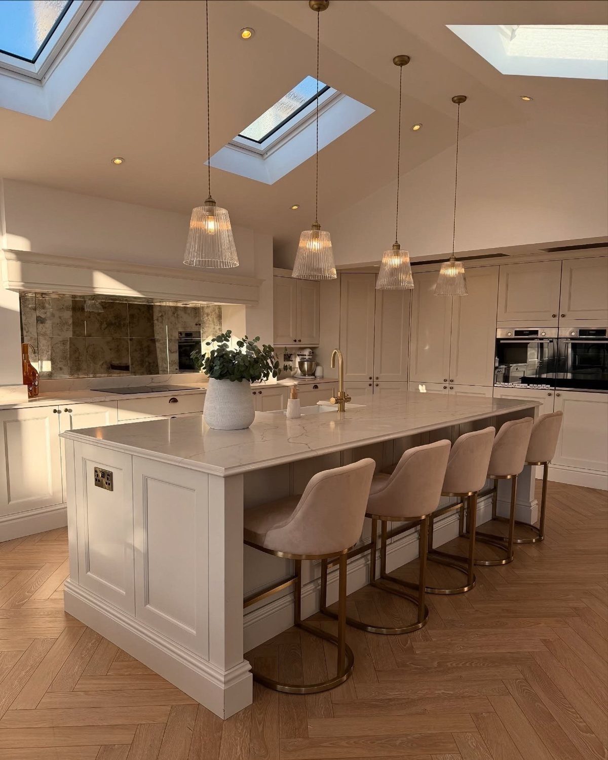 Nigerian Kitchen Design: 25 Ideas for Modern Functional Spaces 9 Four glass pendant lights hanging over a white kitchen island with beige bar stools.