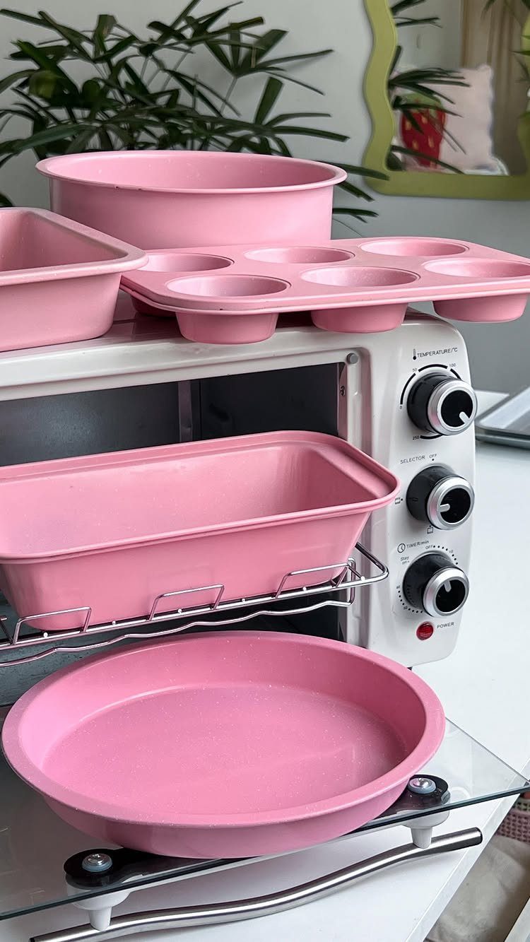 Pink baking pans and a white toaster oven arranged on a kitchen counter.