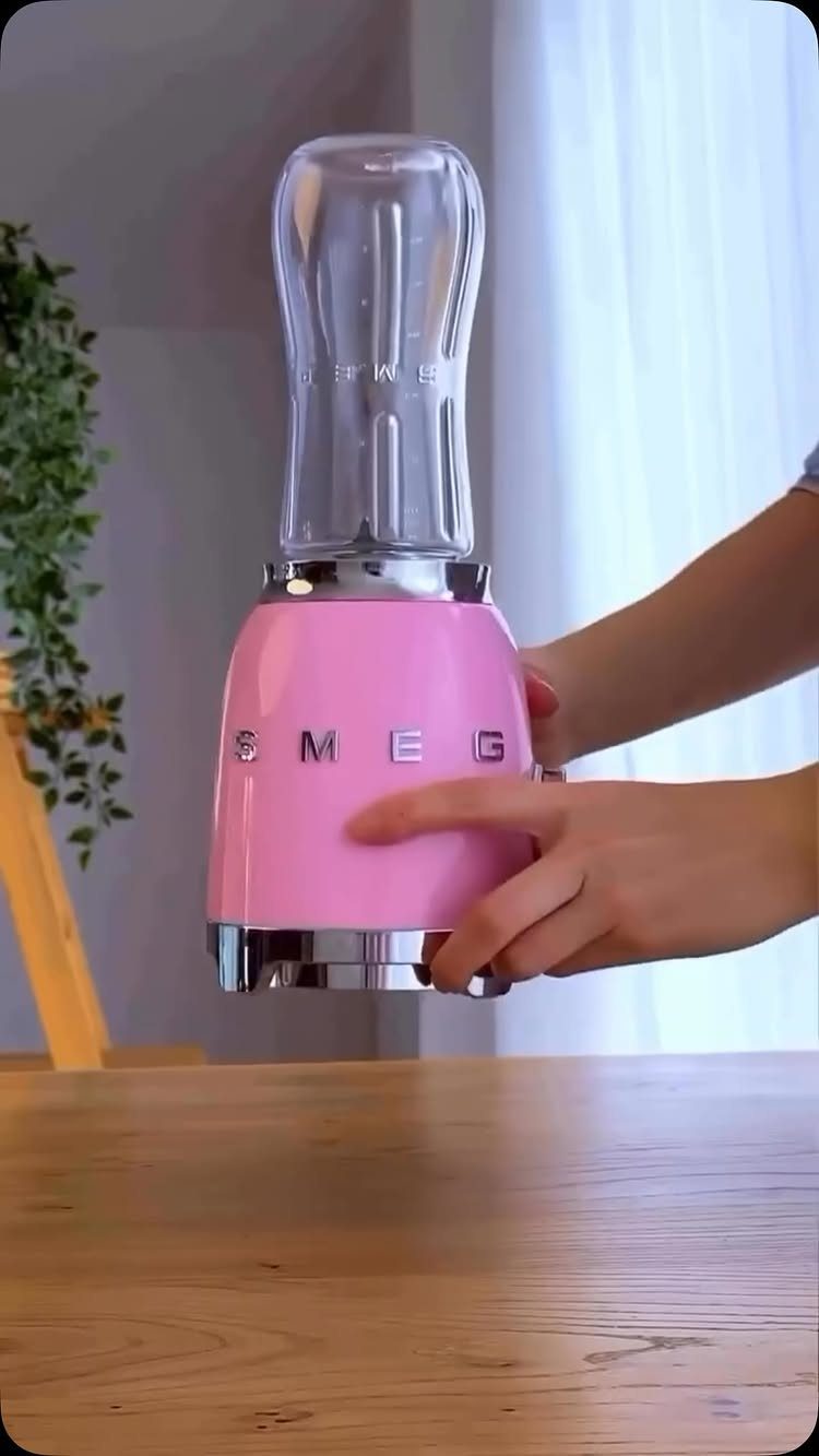 Pink Smeg blender with clear glass jar held by hands on wooden table