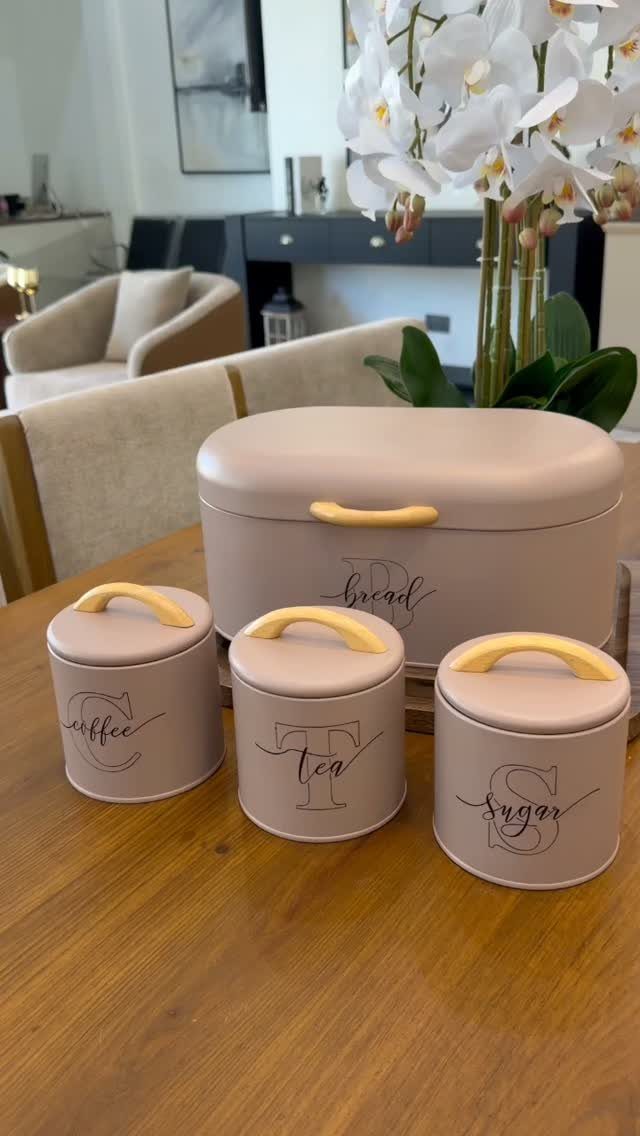 Pale pink bread bin and matching canisters for coffee, tea, and sugar on wood.