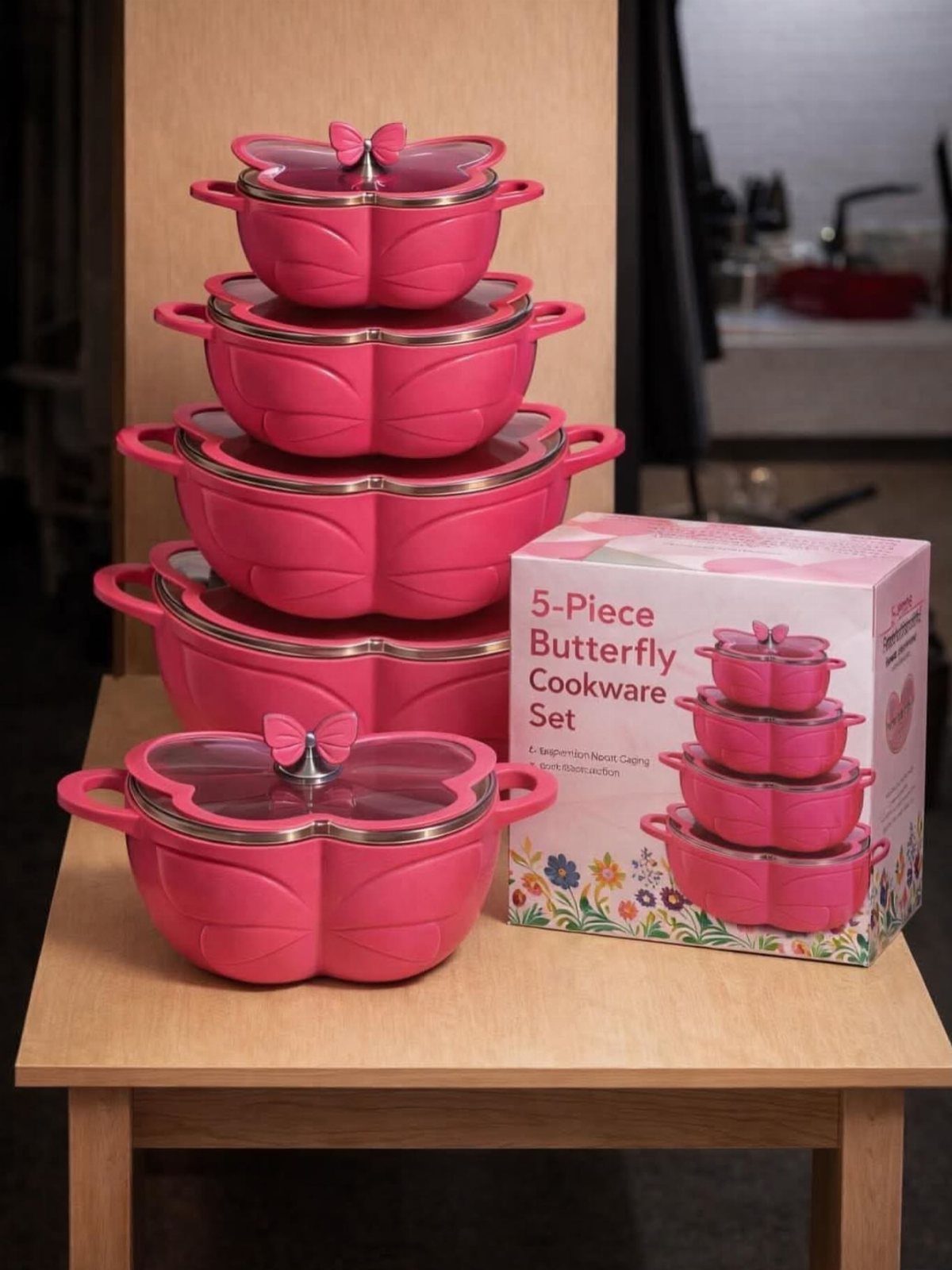 Pink butterfly-shaped cookware pots stacked on a wooden table next to their box.