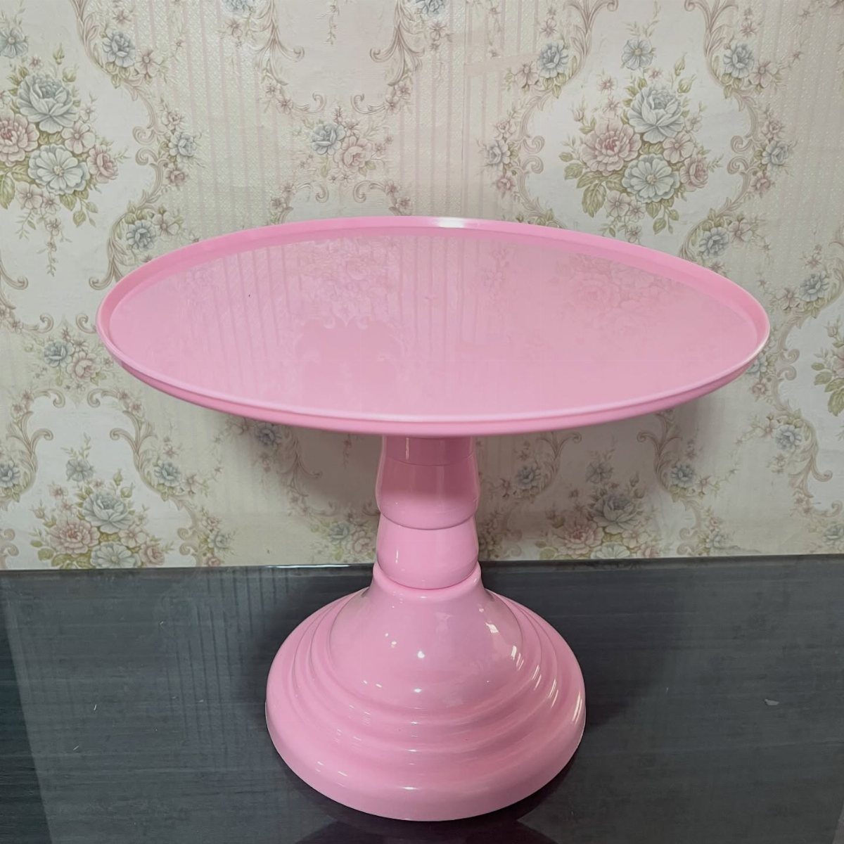 Pink cake stand with a pedestal base against floral wallpaper background.