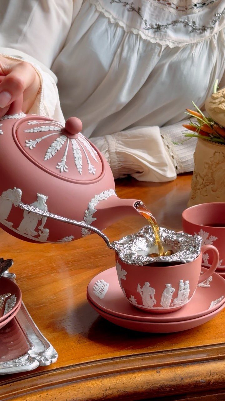 Pink vintage tea set with white relief figures being poured on wooden table