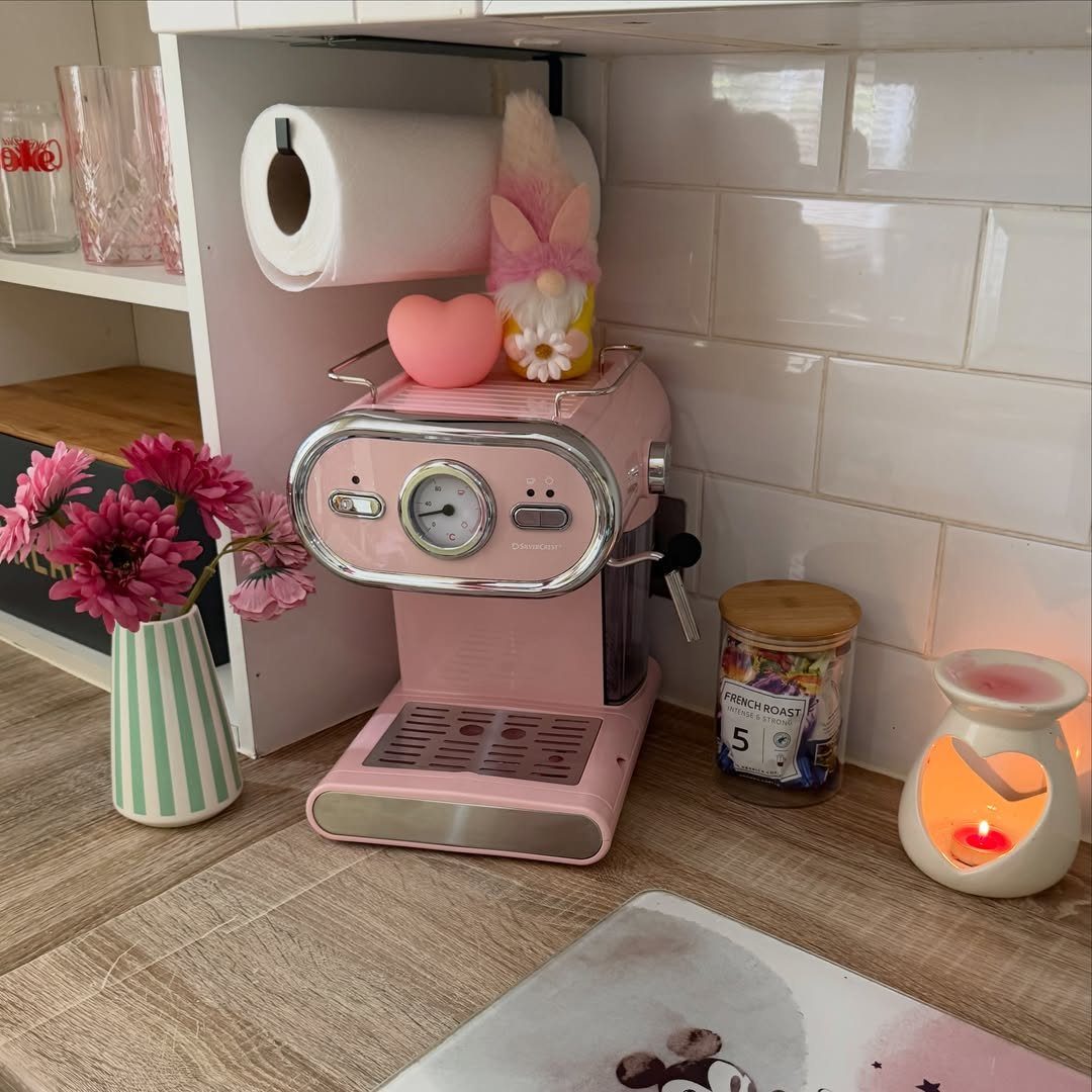 Pink retro espresso machine on a wooden counter with flowers and a gnome.