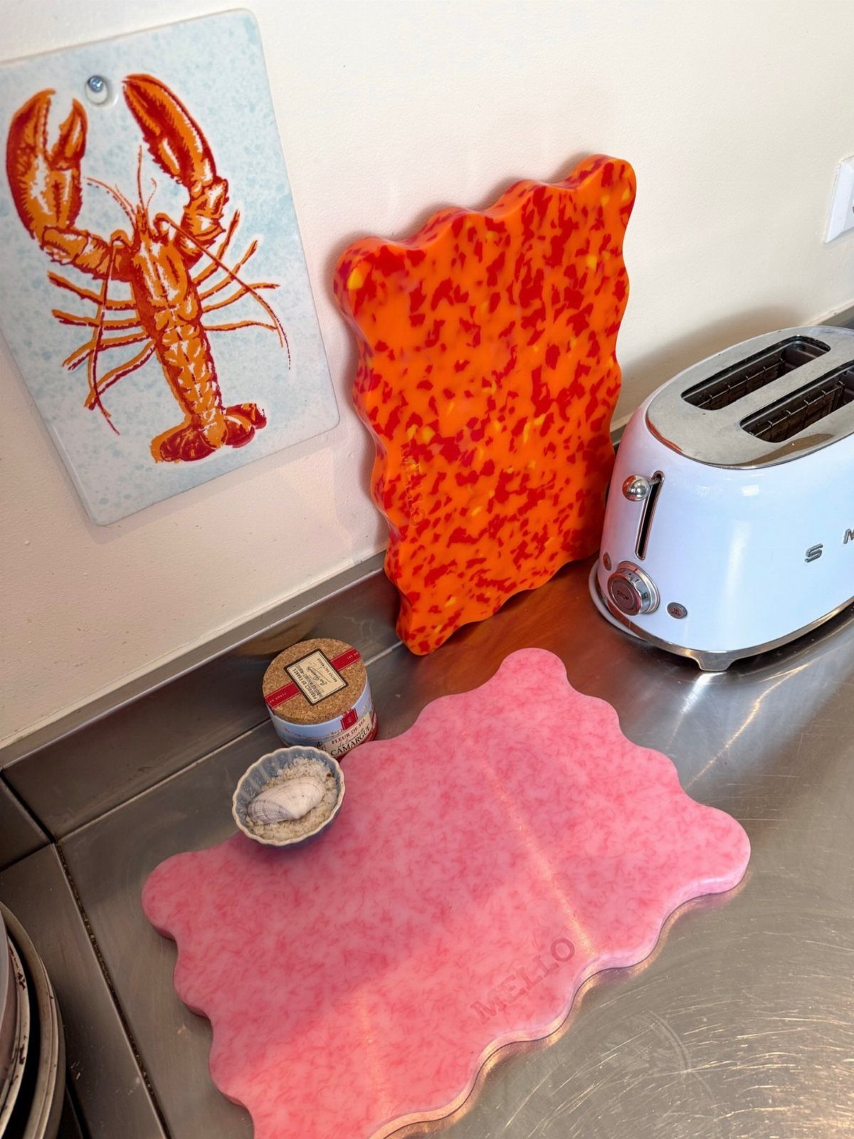 Pink scalloped cutting board on a stainless steel counter next to a white toaster.