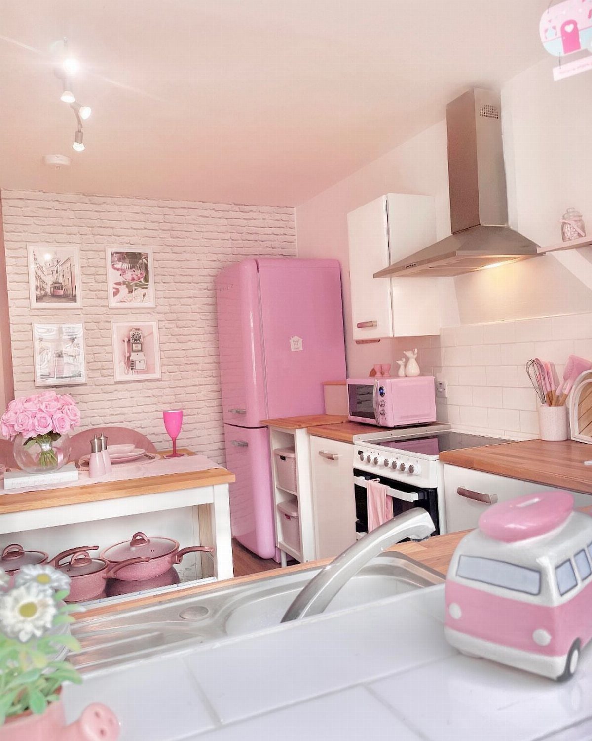 Pink refrigerator and microwave in a bright white kitchen with wooden countertops.