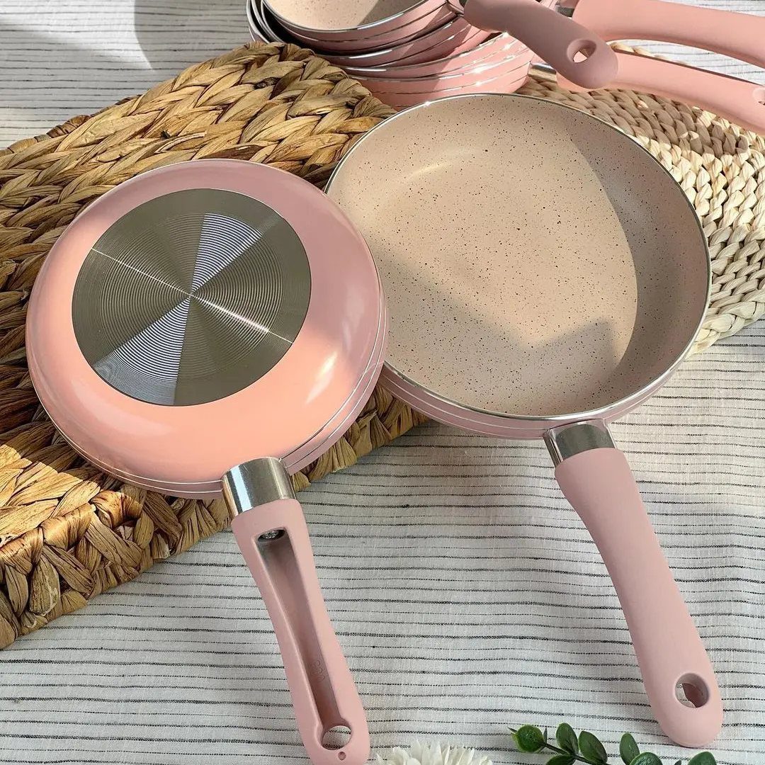 Two pink frying pans with matching handles resting on a woven straw mat.