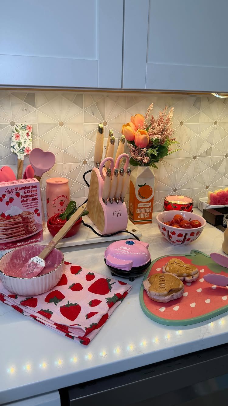 Pink kitchen appliances and accessories arranged on a white countertop with fresh strawberries.