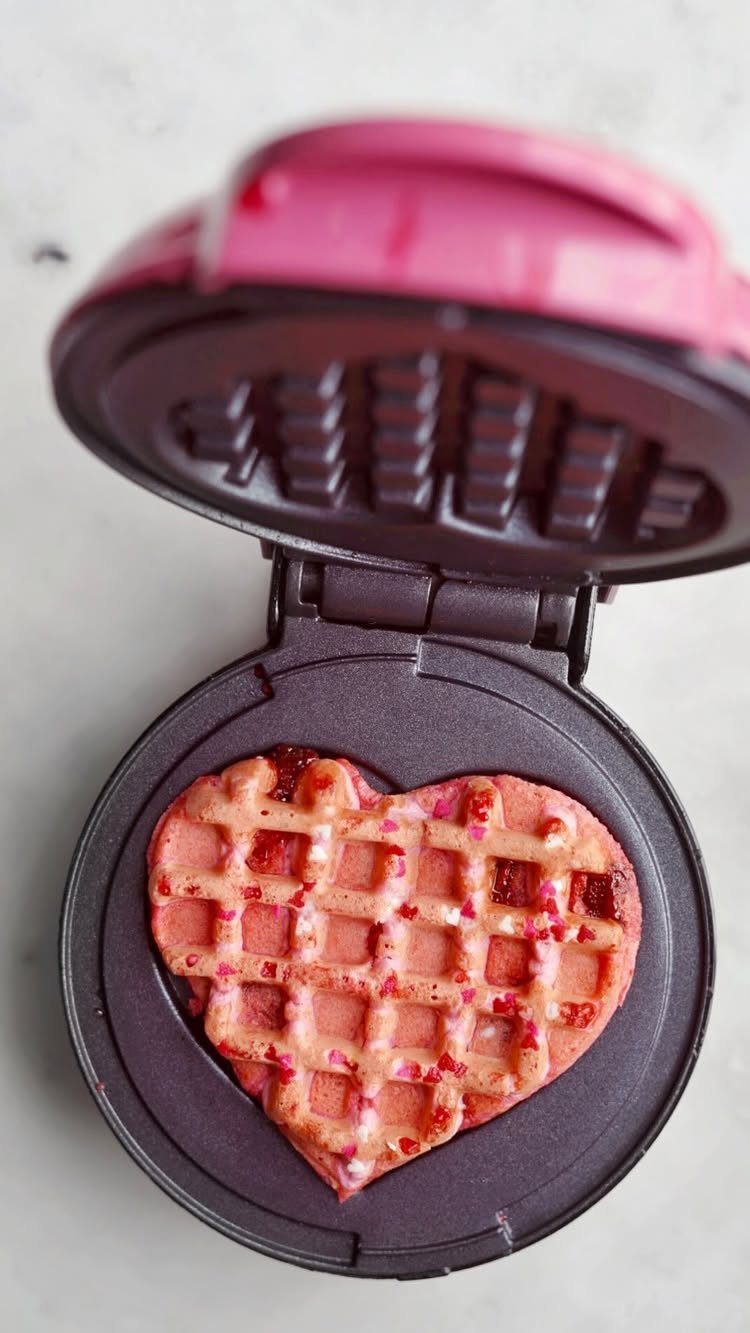 Pink mini waffle maker with a heart-shaped pink berry waffle inside.