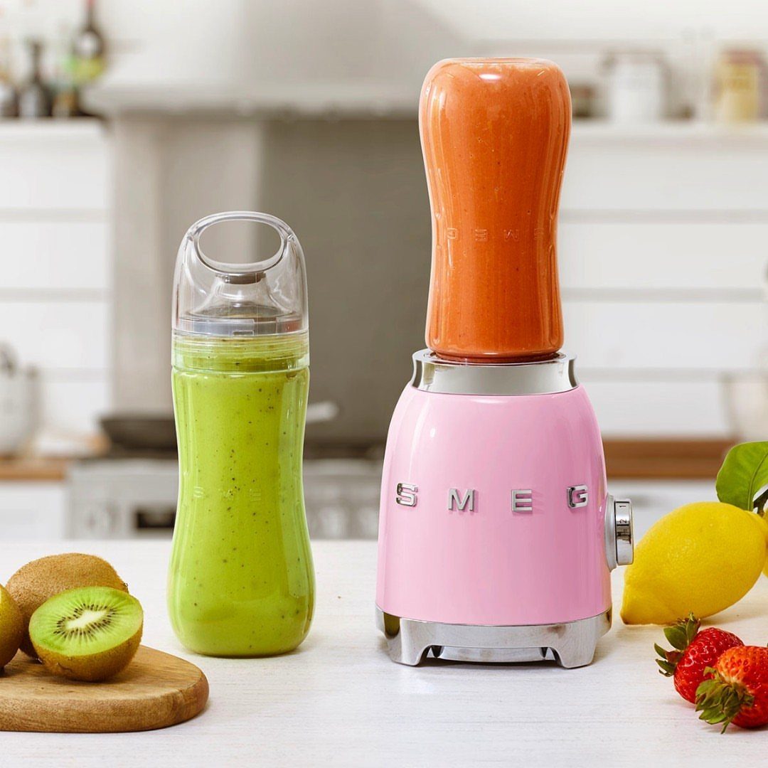 Pink personal blender with orange smoothie and a green smoothie bottle on counter