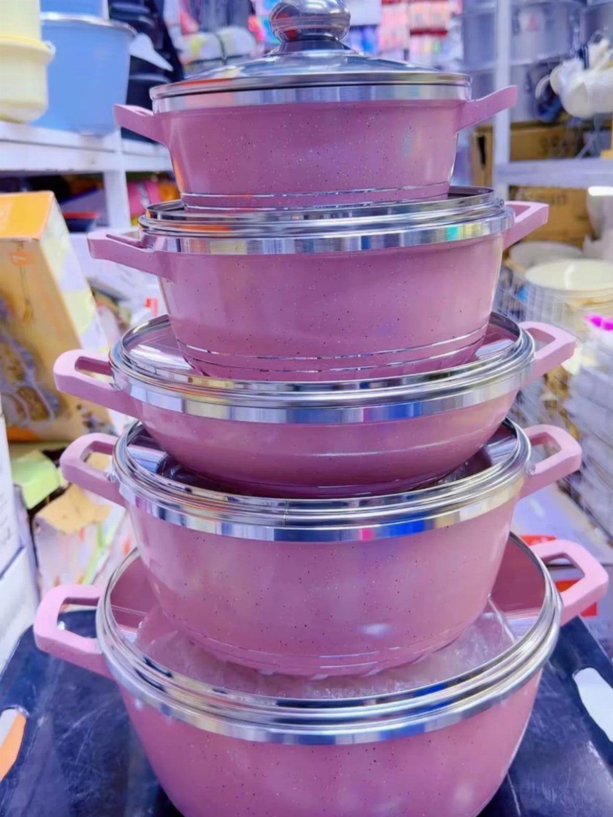 Stacked pink pots with silver lids and handles in a retail store.