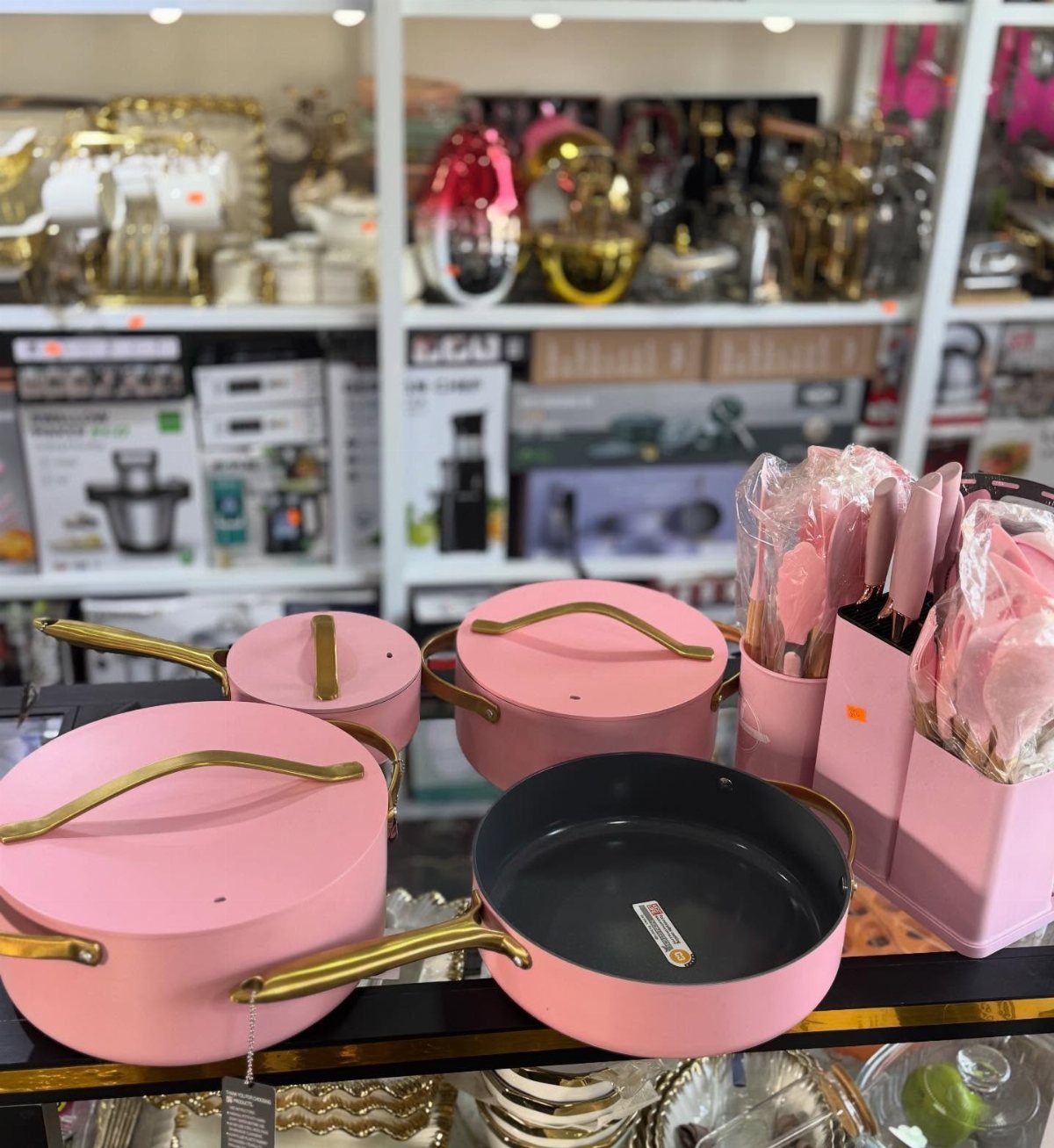 Pink pots and pans with gold handles displayed on a store shelf.