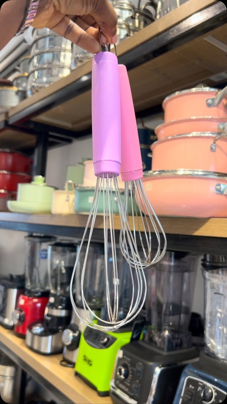 Two pink whisks with silicone handles held up in a kitchenware store.