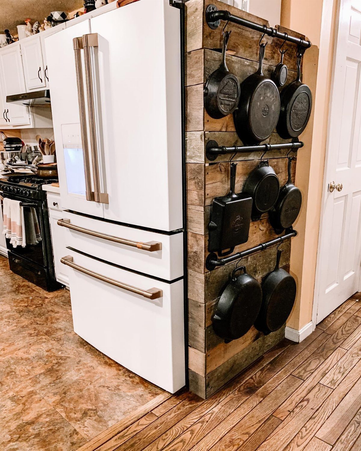 Cast iron skillets hanging from black metal pipes on a rustic wooden wall.