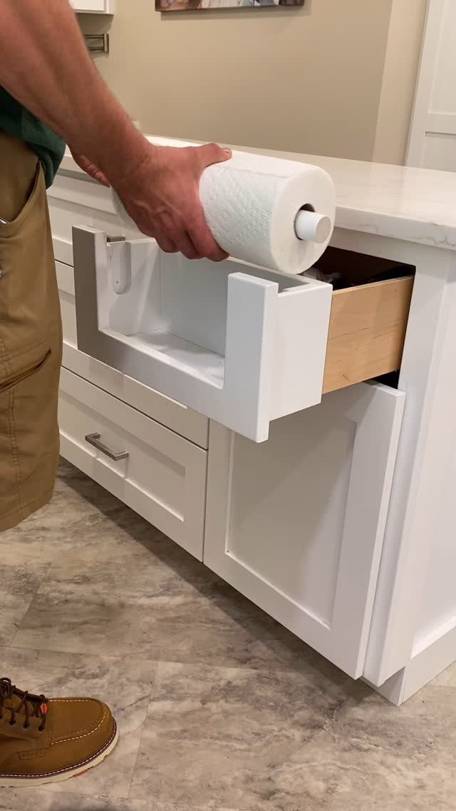White kitchen drawer being pulled out to reveal a paper towel roll inside.