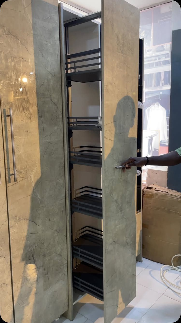 Nigerian Kitchen Design: 25 Ideas for Modern Functional Spaces 22 Pull-out metal wire pantry shelves inside a tall grey textured kitchen cabinet.