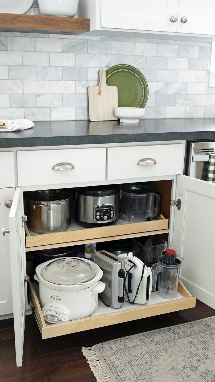 Pull-out wooden shelves in a white kitchen cabinet storing various small electrical appliances.