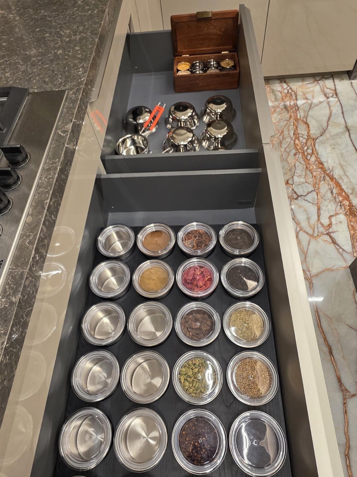 Narrow pull-out kitchen drawer filled with organized small metal spice containers and lids.