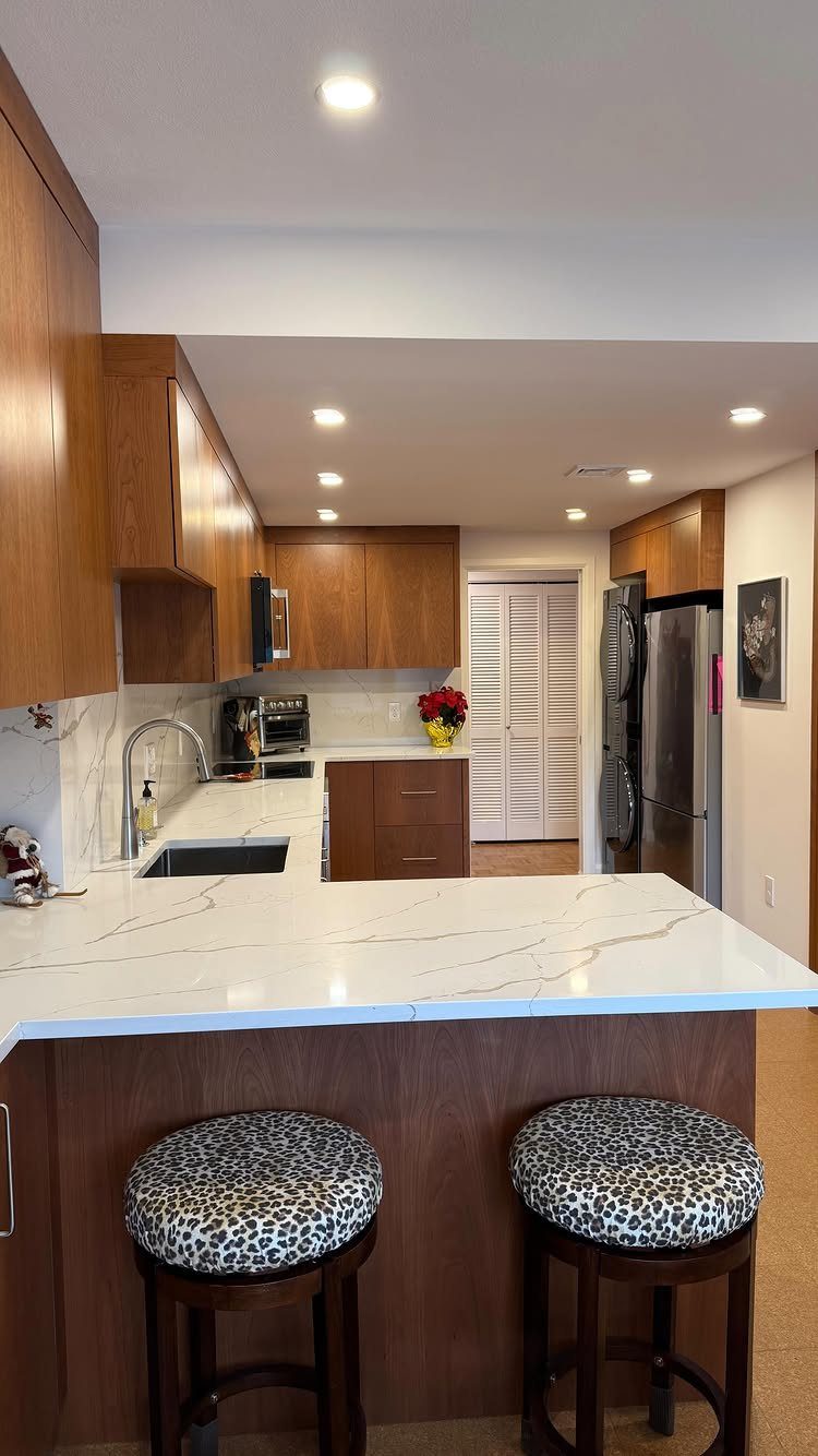 Nigerian Kitchen Design: 25 Ideas for Modern Functional Spaces 26 White marble-patterned quartz countertops in a kitchen with brown wooden cabinets and stools.