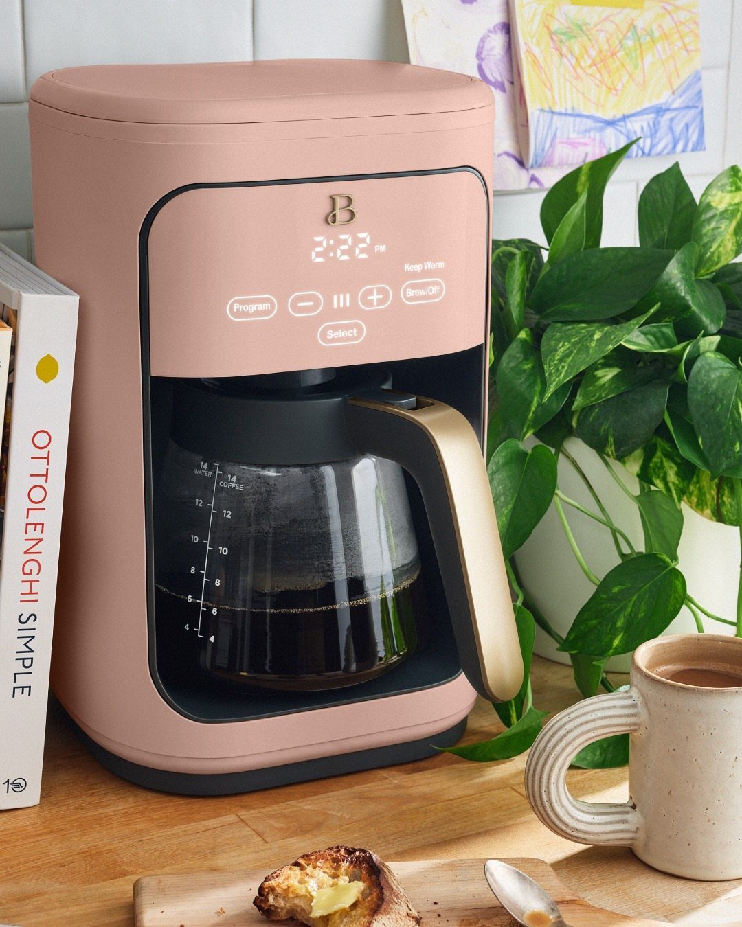Rose gold filter coffee maker with a glass carafe on a wooden kitchen counter.