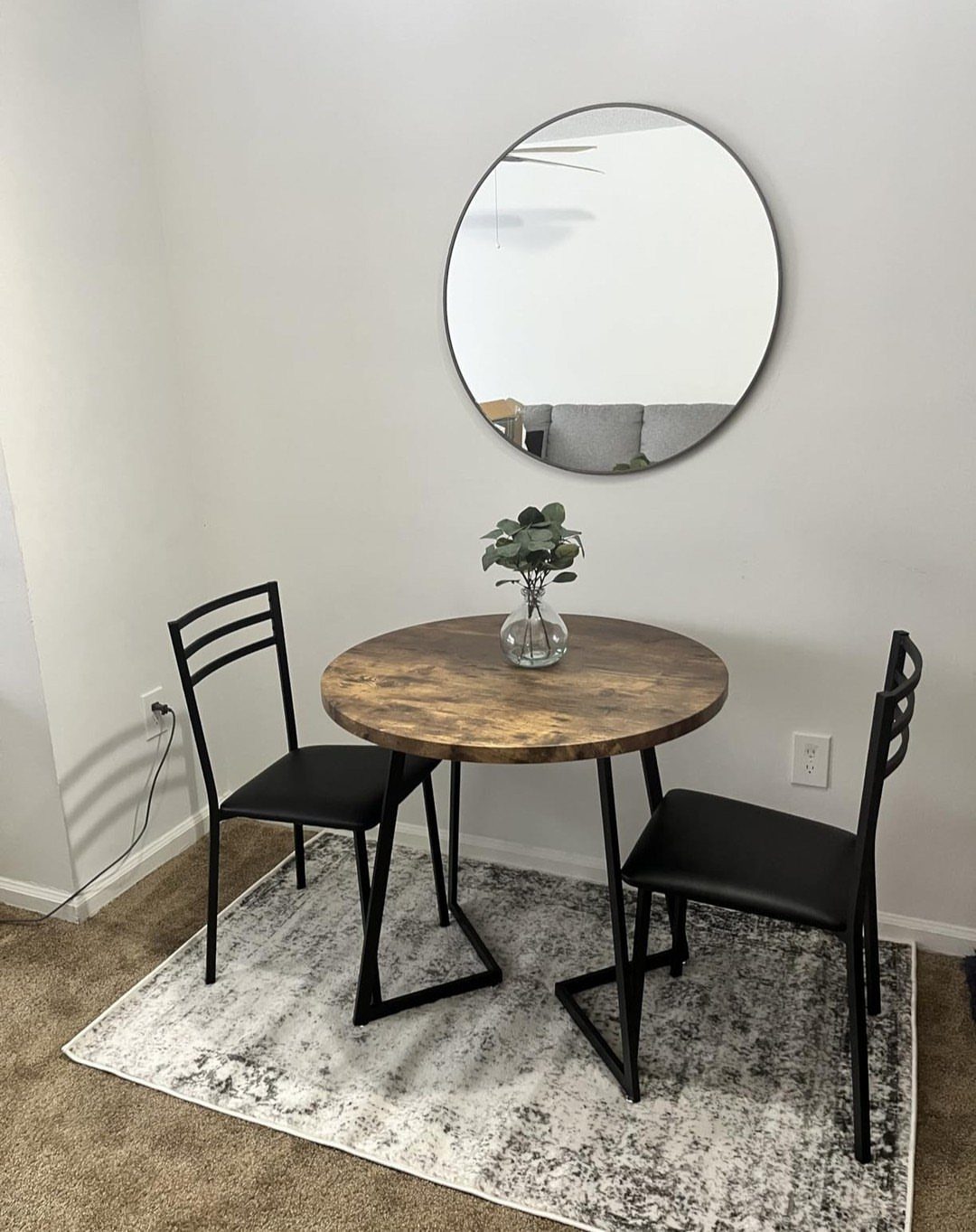 Round wooden dining table with two black chairs and a circular wall mirror.