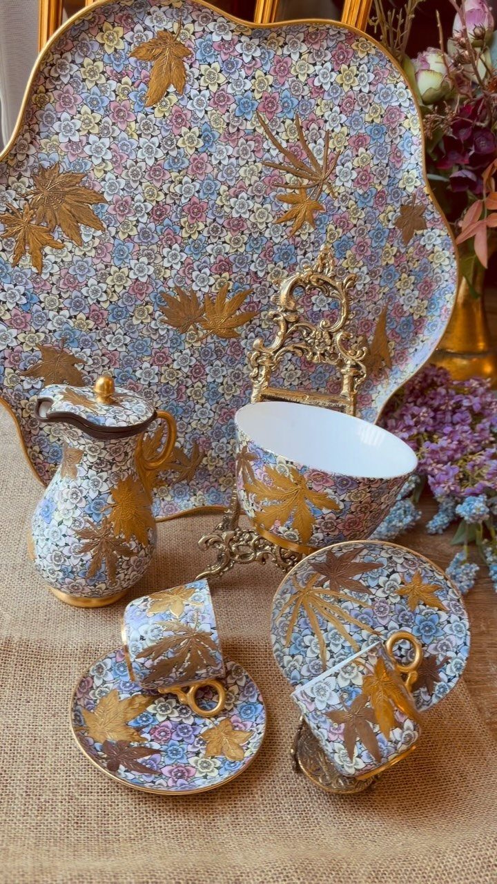 Ornate porcelain tea set with gold leaf and floral patterns on a burlap surface.