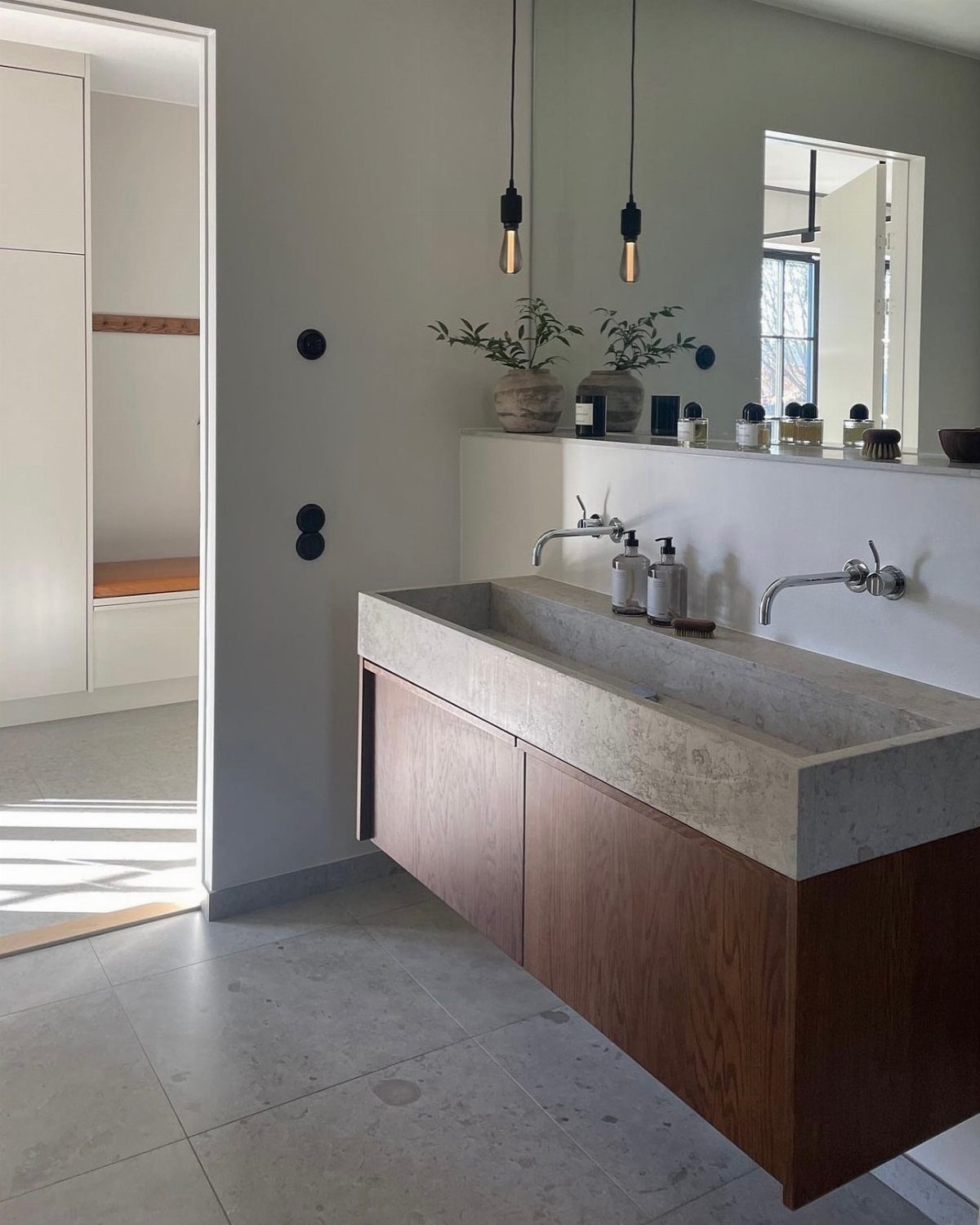 Concrete trough sink with wooden cabinets in a minimalist Scandinavian style bathroom.