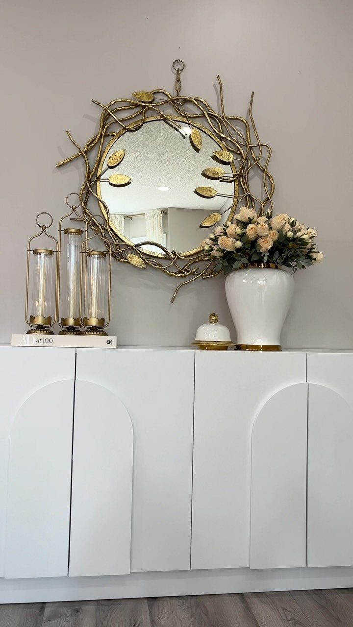 Living Room Storage Cabinet Ideas: 14 Styles That Fit Any Space 2 White sideboard cabinet with arched doors and gold decor under a branch-style mirror.