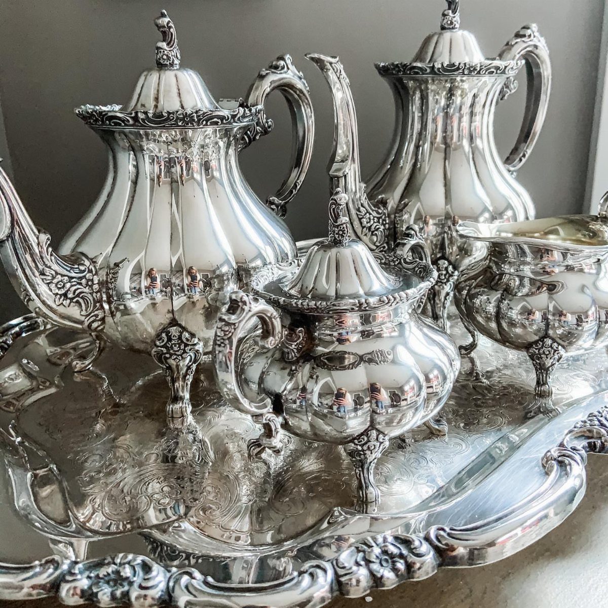 Ornate silver tea service with teapot and tray on a neutral background.