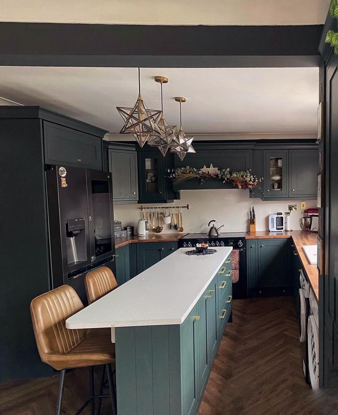 Slim dark green kitchen island with white countertop and brown leather bar stools.