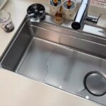 Stainless steel single-bowl kitchen sink with chrome faucet and light-colored countertop.
