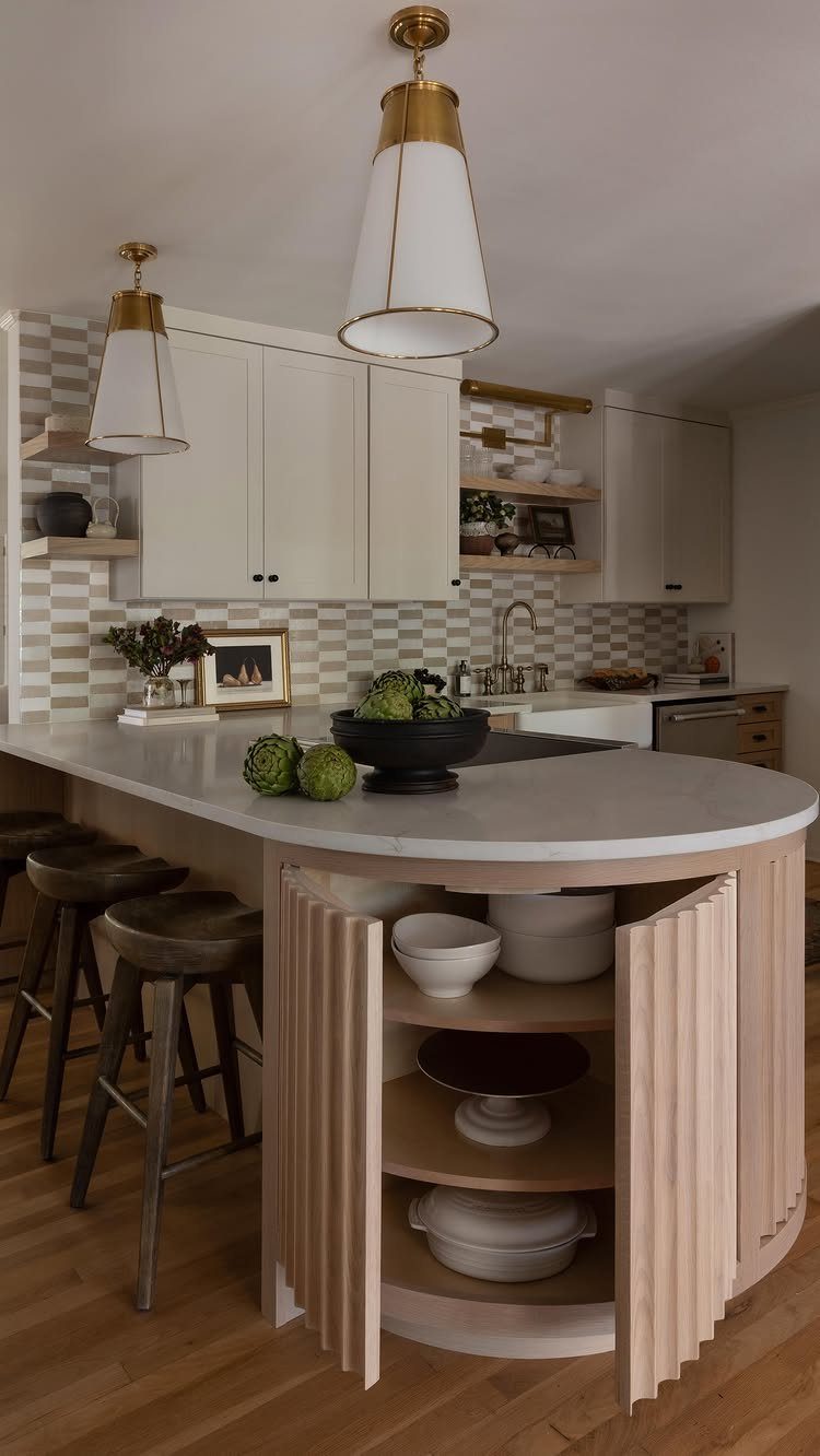 Small white kitchen with marble peninsula, wooden stools, and gold pendant lighting.