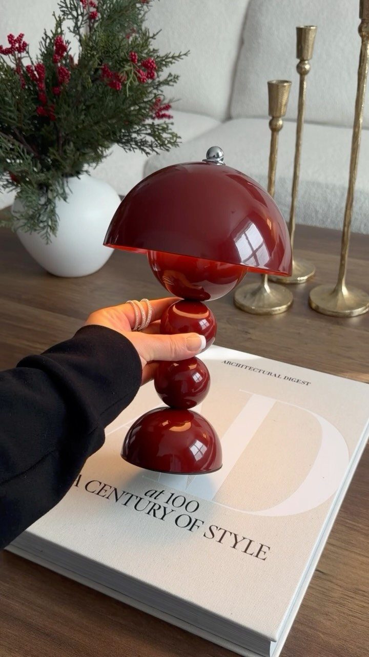 Glossy red mushroom table lamp held over a white design book on wooden table.