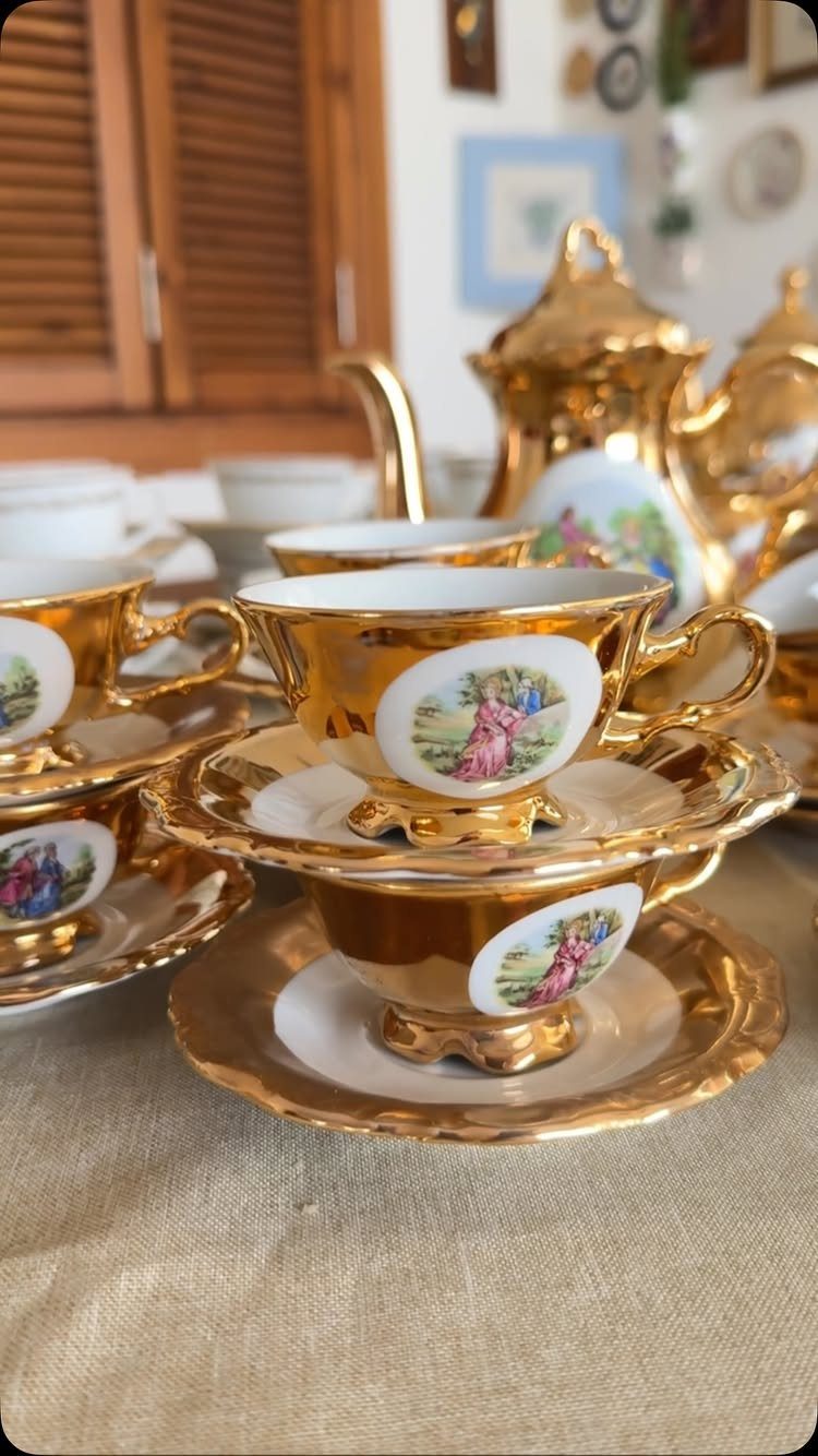 Gold-plated porcelain tea set with painted floral medallions on a beige linen tablecloth.