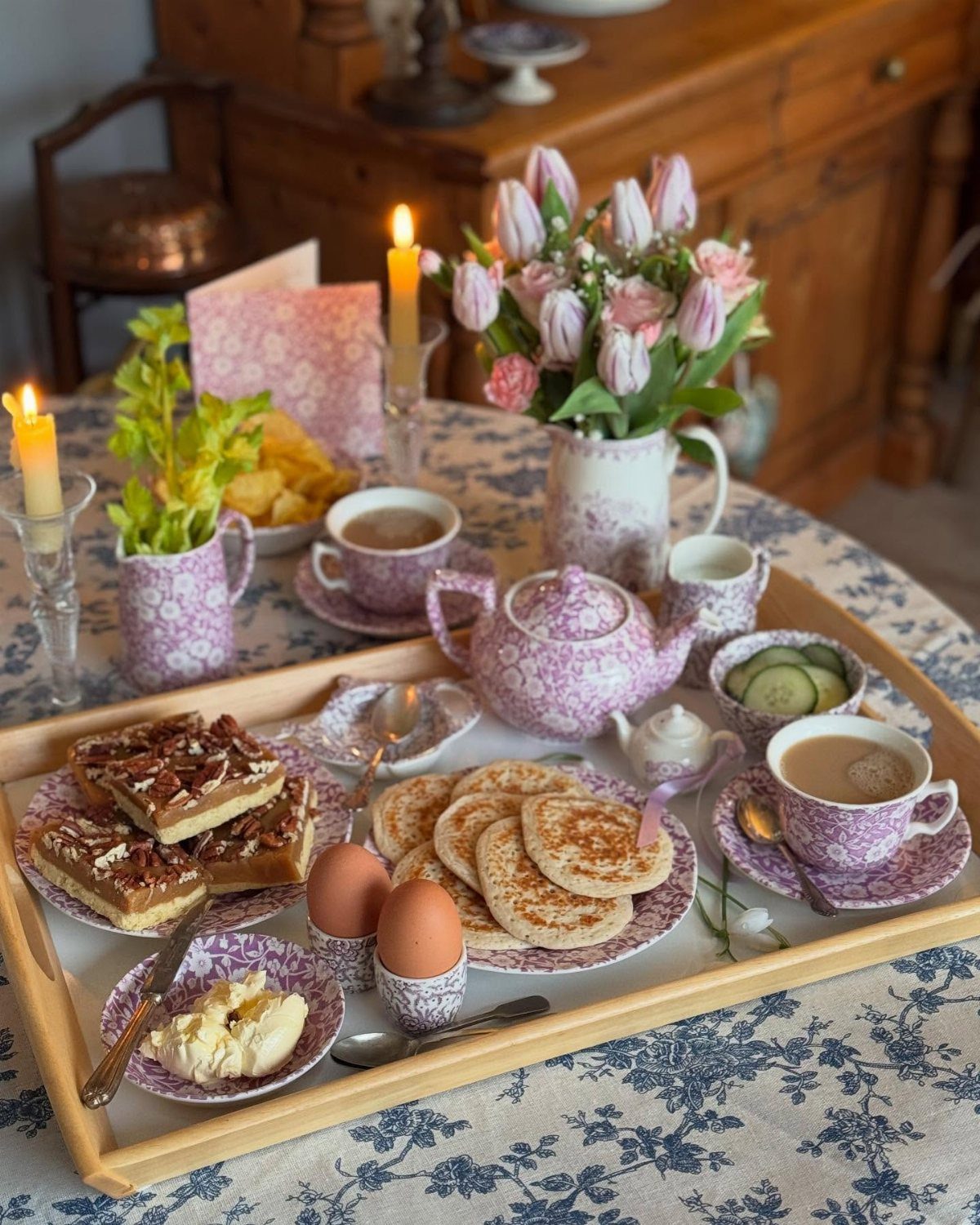 Floral porcelain tea set and breakfast foods arranged on a light wooden serving tray.