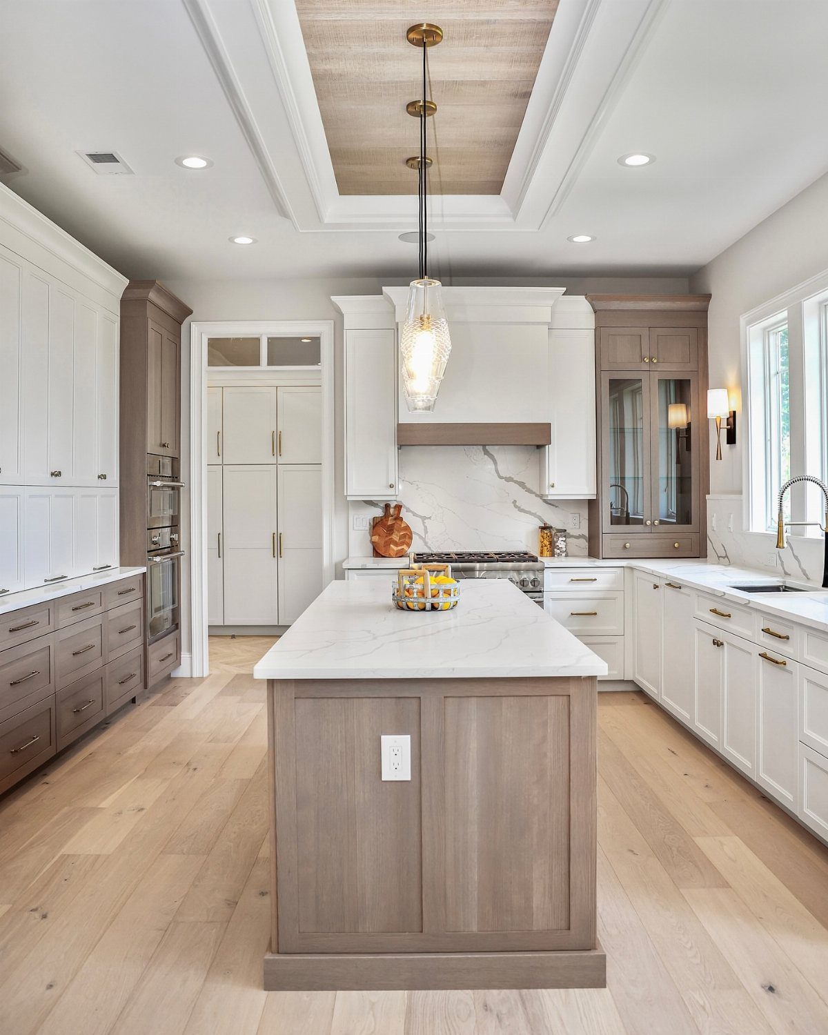 Two-tone white and grey-brown kitchen cabinets with gold hardware and white marble island.
