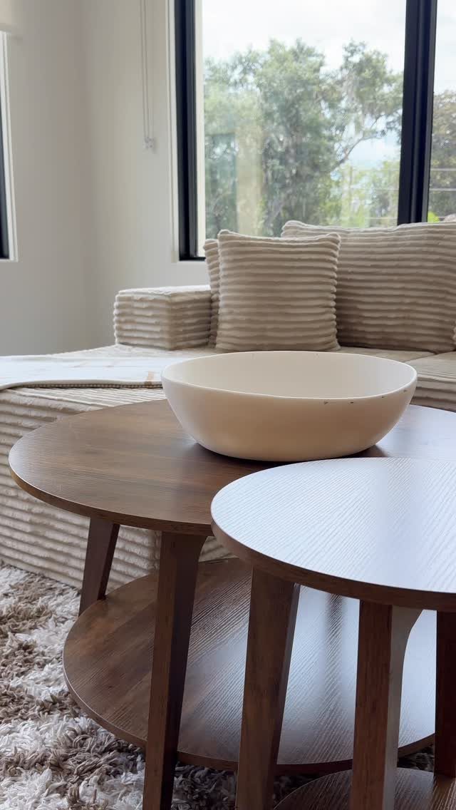 Two round wooden nesting tables with a cream bowl in a modern living room.