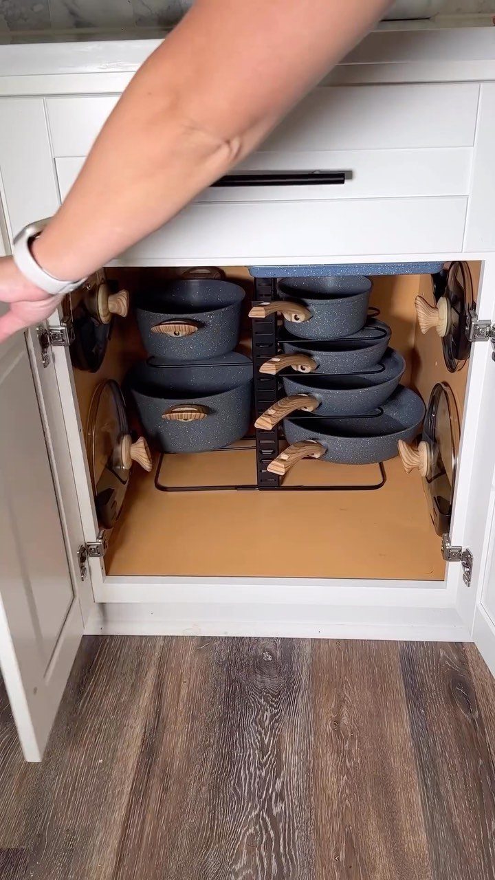 Grey pots and pans stored vertically in a black wire organizer inside a cabinet