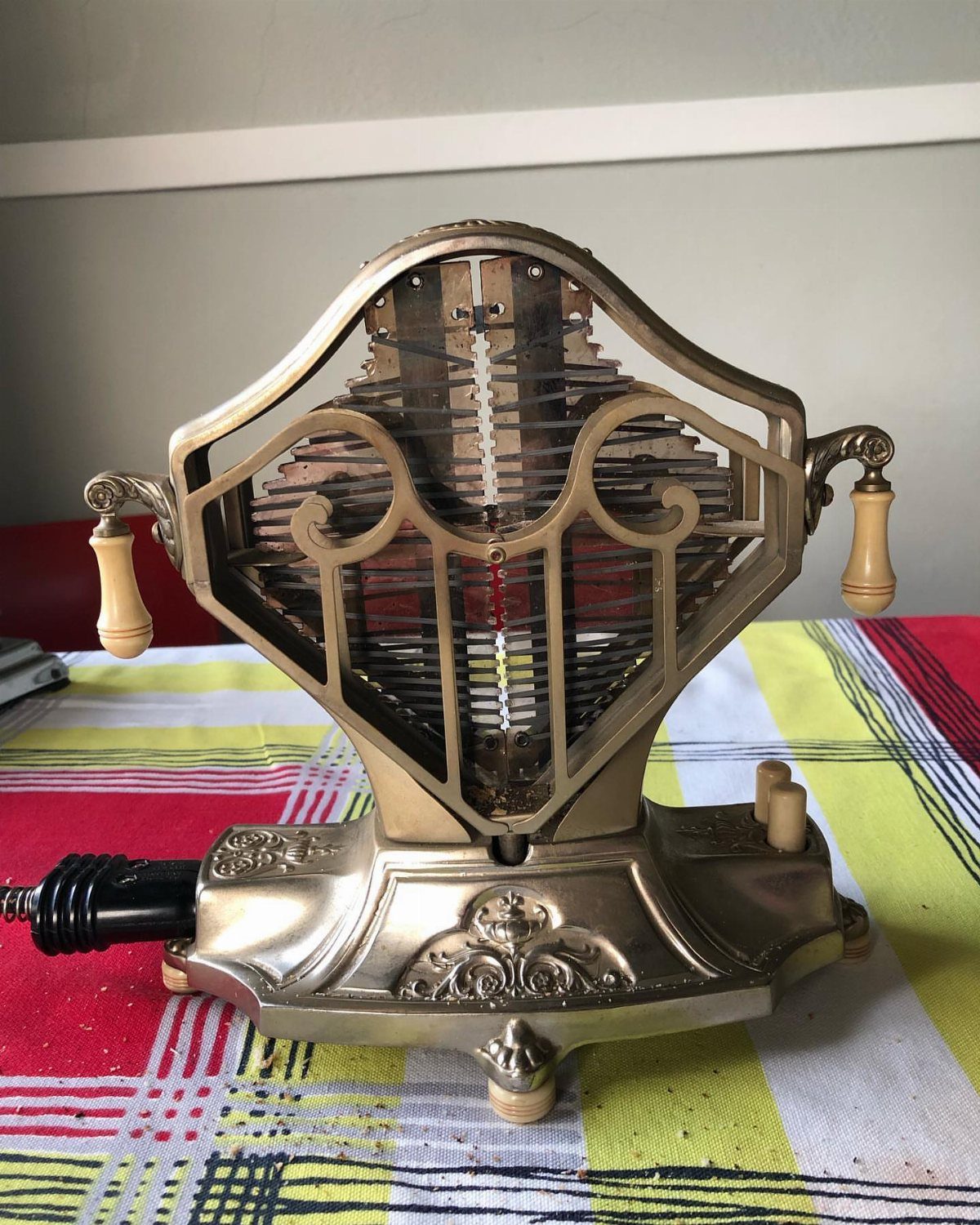 Ornate gold vintage toaster with decorative scrolls on a checkered tablecloth.