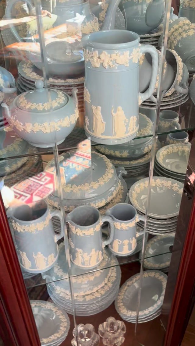 Light blue Wedgwood Jasperware pottery with white relief figures displayed in a glass cabinet.