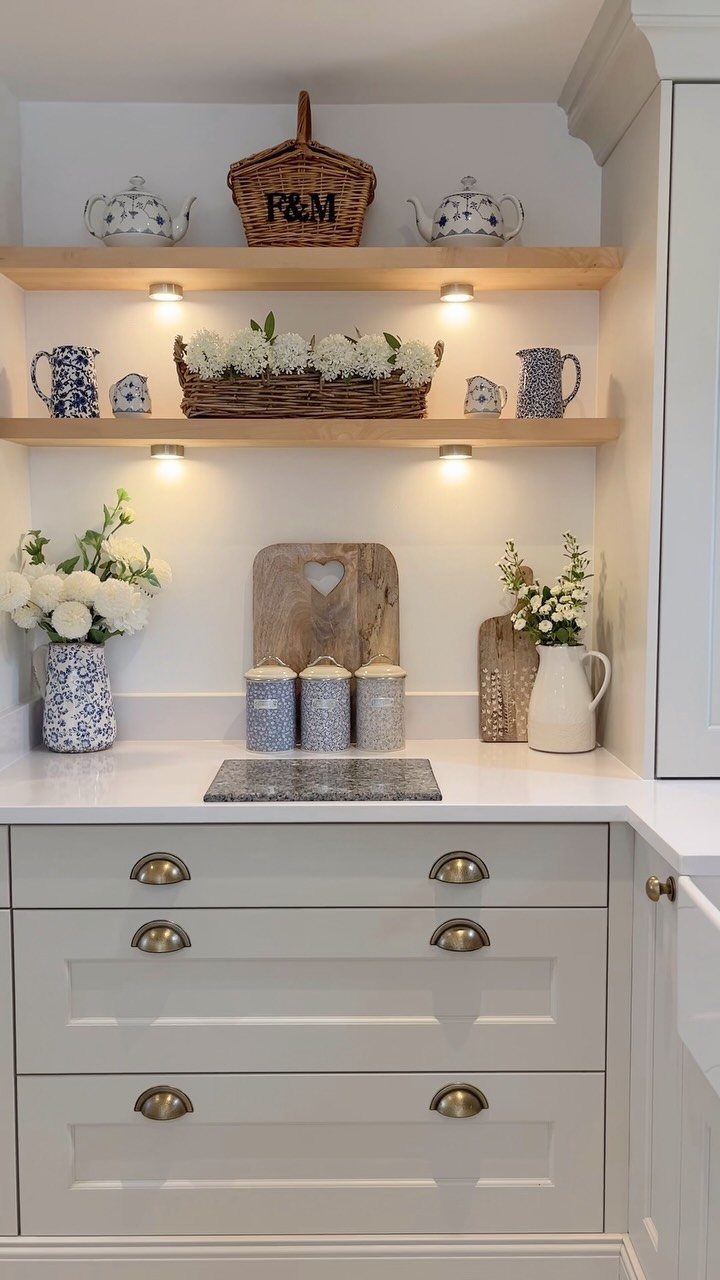 White kitchen cabinets with gold cup pulls and open wooden shelving above.